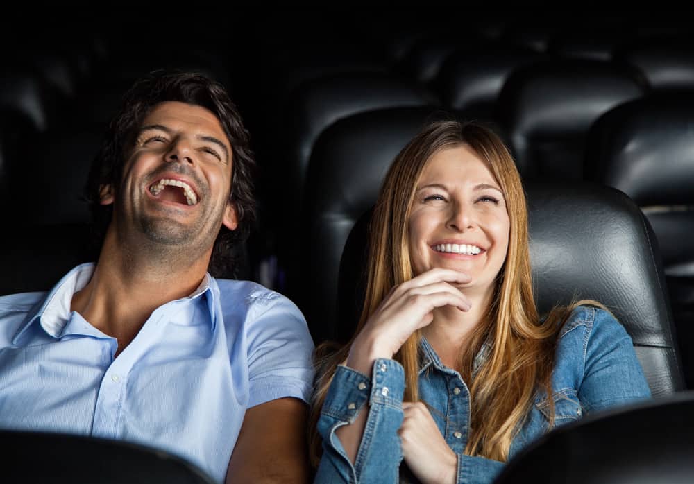un homme et une femme sont assis en train de regarder un film et de rire