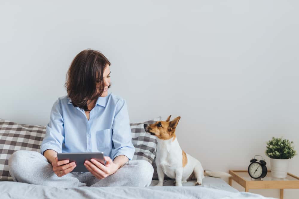 une femme avec un chien est assise sur le lit