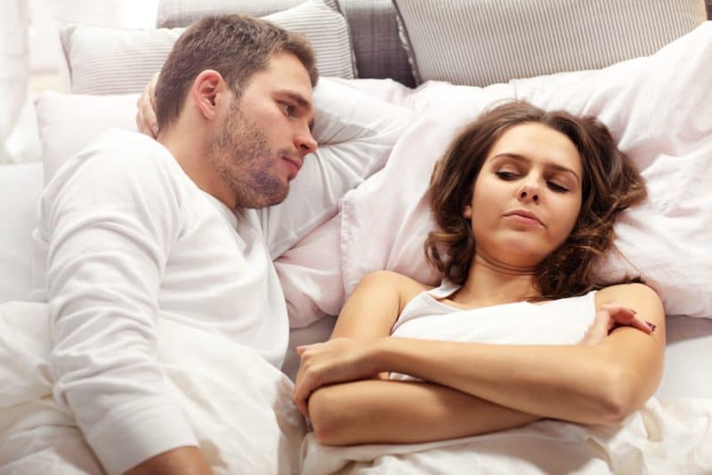 une femme en colère est allongée dans son lit pendant qu'un homme la regarde
