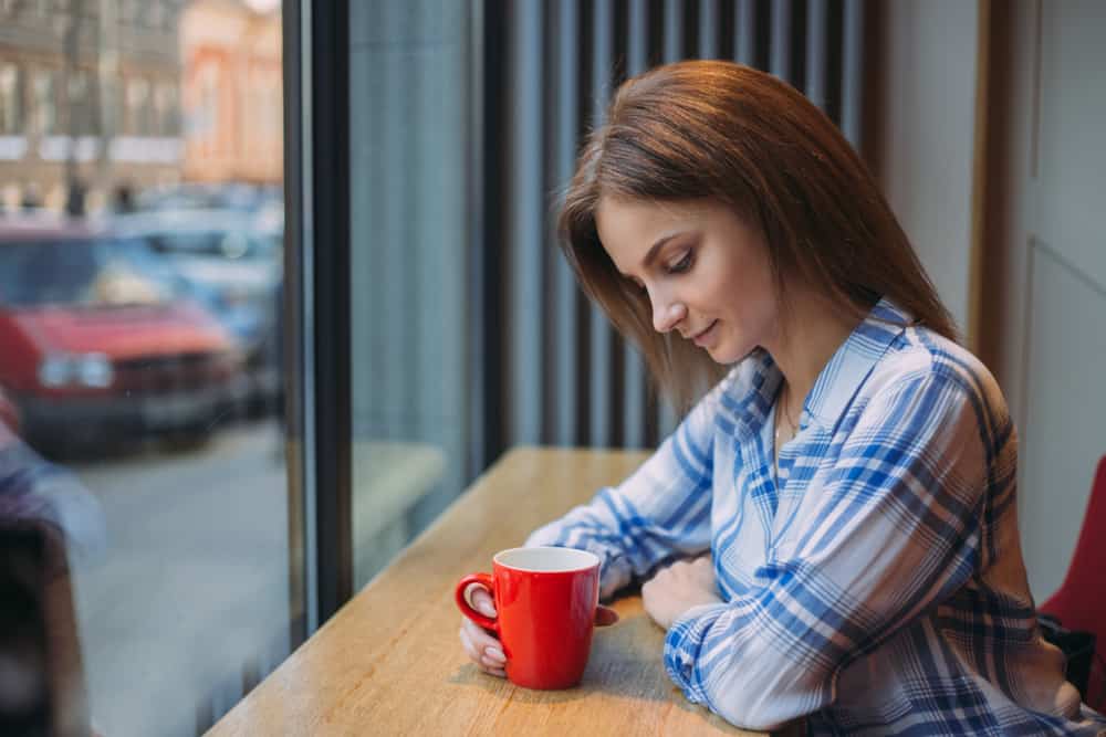 une femme imaginaire est assise à une table et boit du café