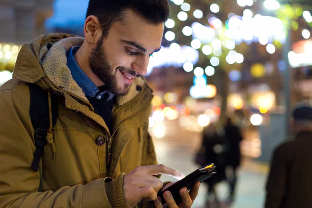 à l'extérieur se trouve un homme souriant dans une veste marron et textos sur son smartphone