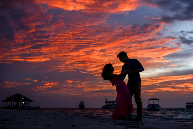 un homme et une femme dansent sur une plage de sable au coucher du soleil