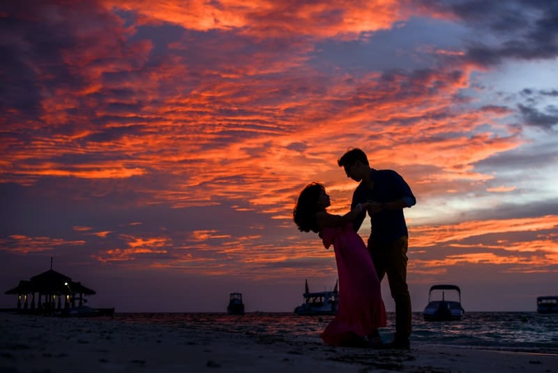 un homme et une femme dansent sur une plage de sable au coucher du soleil
