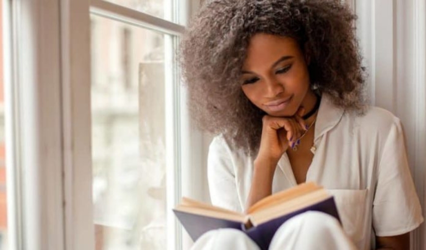 une femme aux cheveux crepus est assise pres de la fenetre et lit un livre