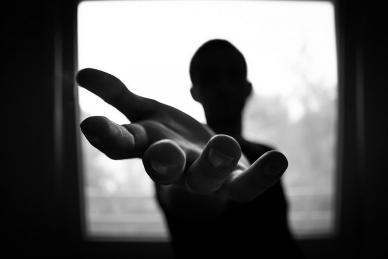 un homme près de la fenêtre dans le noir se tient les bras tendus