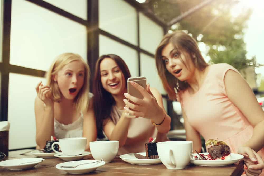 Des amis sont assis en train de boire du café en train de manger un gâteau et de se demander quelque chose au téléphone
