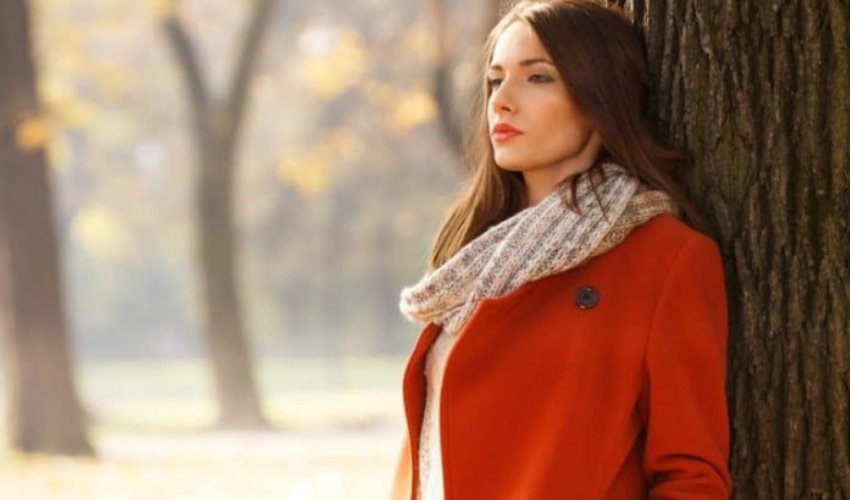 une femme en manteau rouge appuyee contre un arbre