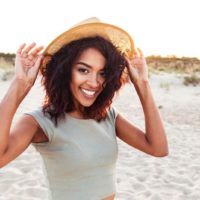 femme heureuse avec chapeau posant sur le sable