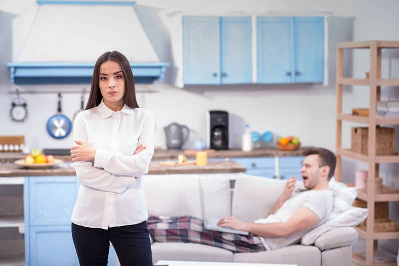 Femme en colère debout tandis que l'homme allongé sur le canapé