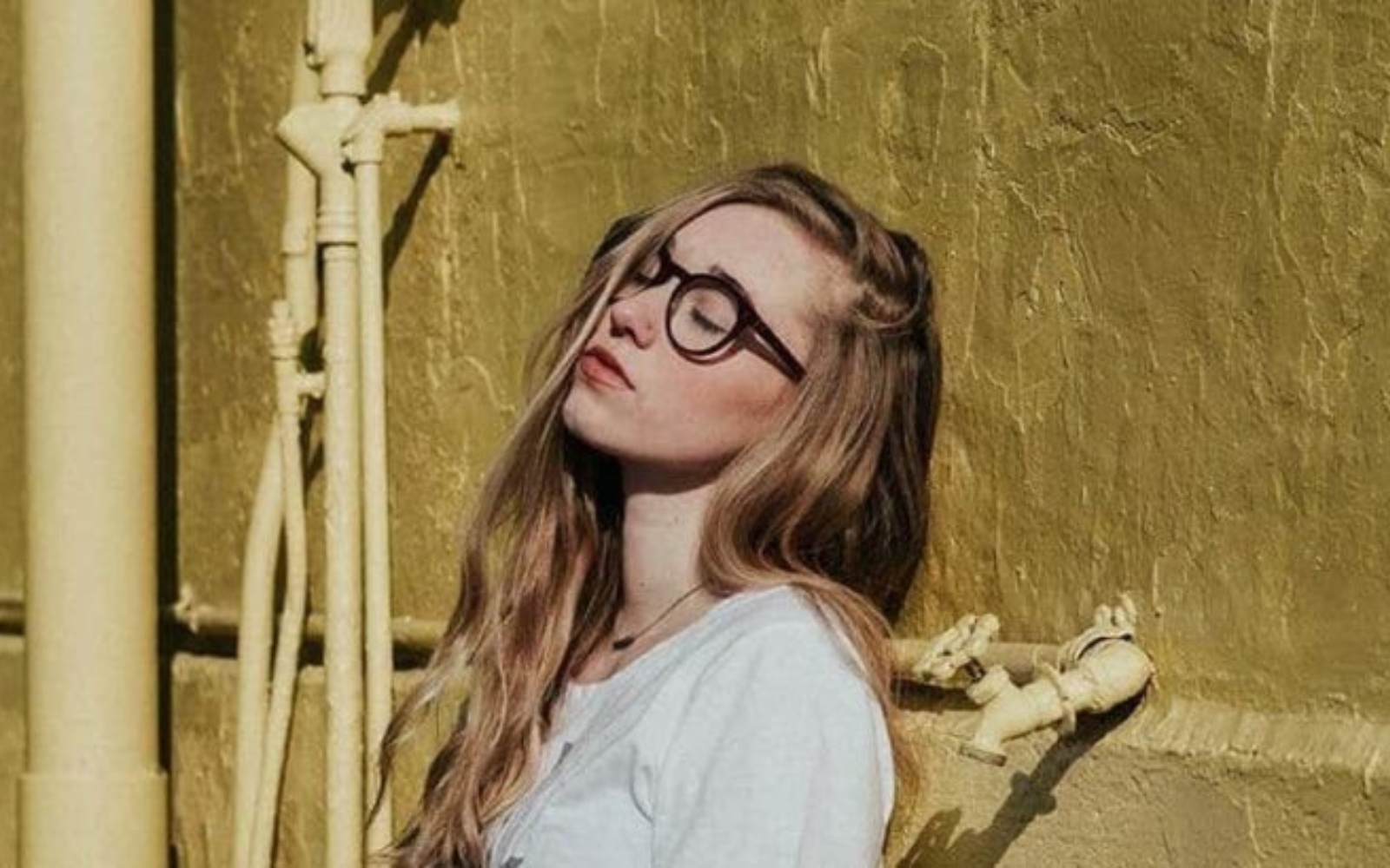 une femme brune avec des lunettes appuyee contre le mur