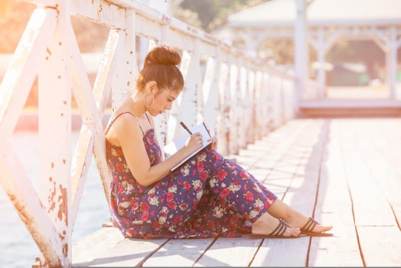 une femme est assise près du pont et écrit une lettre