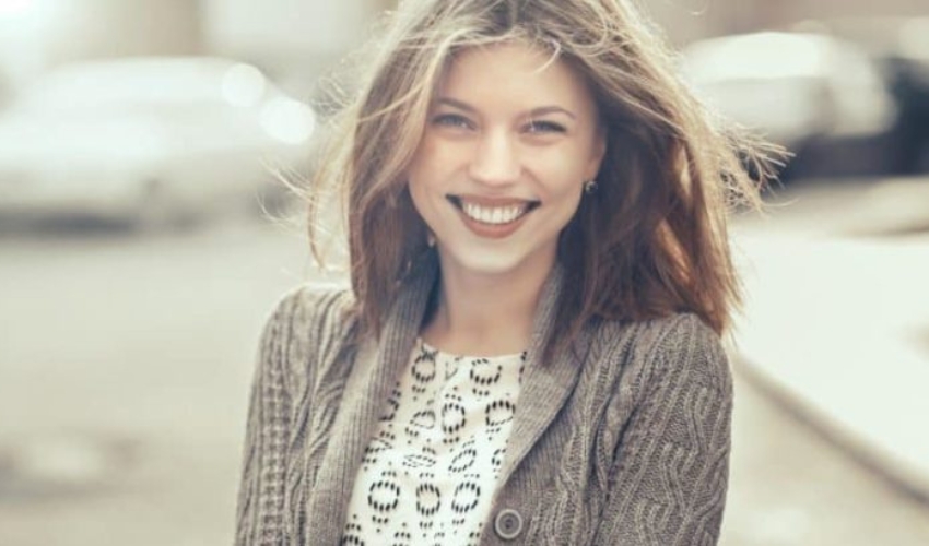 une femme aux cheveux bruns avec un pull sourit