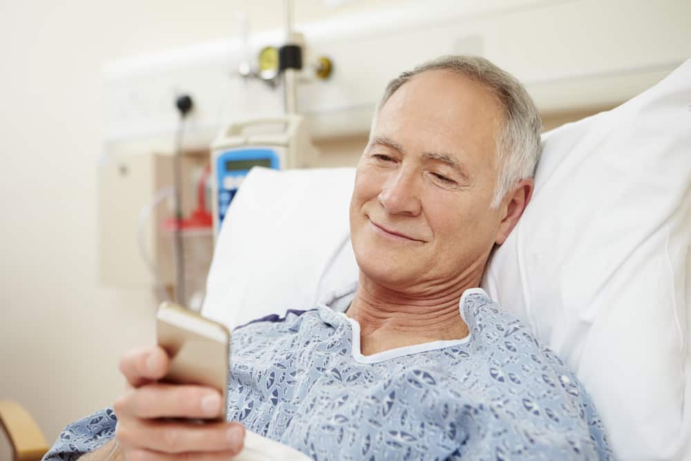 Un homme âgé dans un lit d'hôpital lit un sms avec un sourire