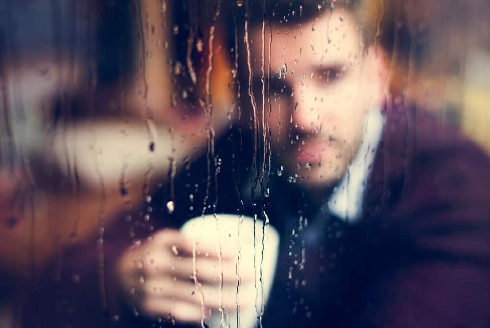 Un homme buvant du café en regardant par la fenêtre alors que la pluie tombe