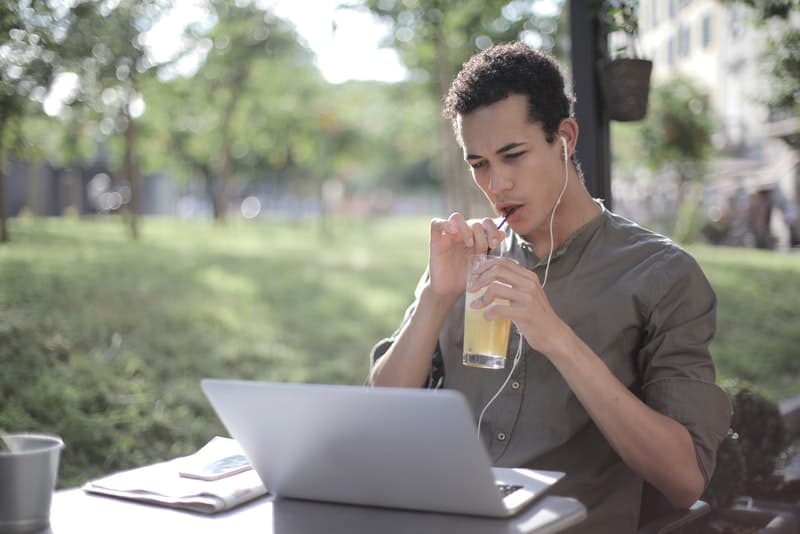 Un homme buvant du jus et regardant quelque chose sur un ordinateur portable avec des écouteurs dans ses oreilles