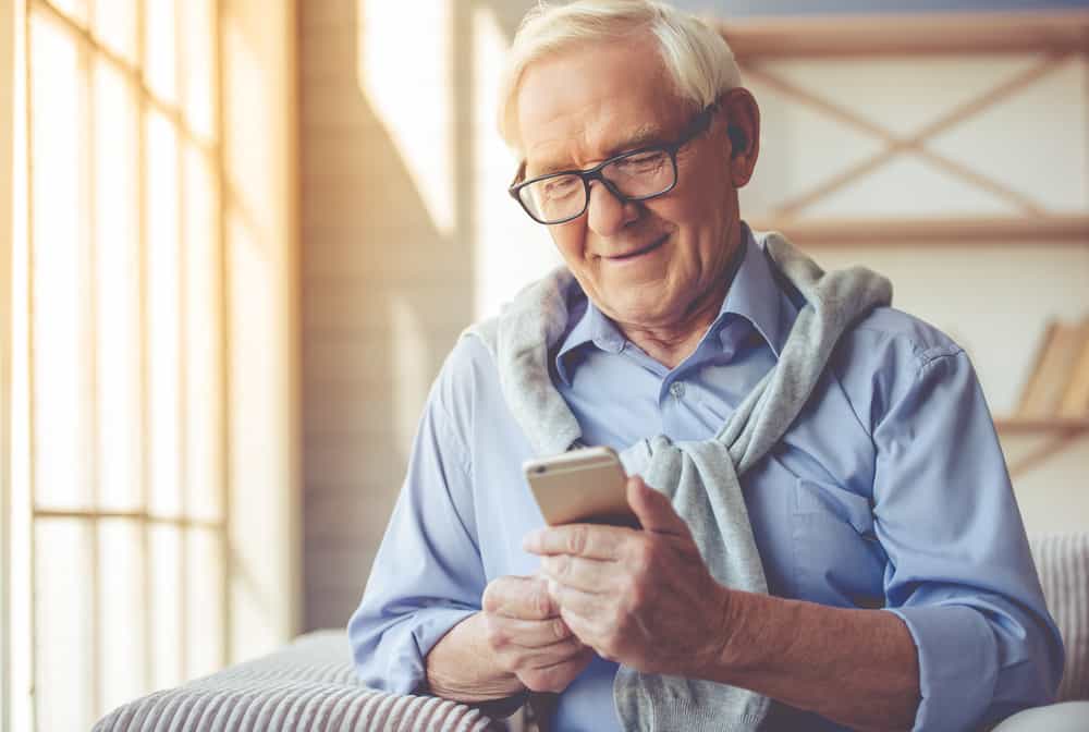 Un homme plus âgé souriant lit un message sur son téléphone portable
