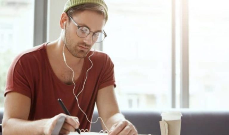 un homme avec des ecouteurs dans les oreilles sassied et ecrit