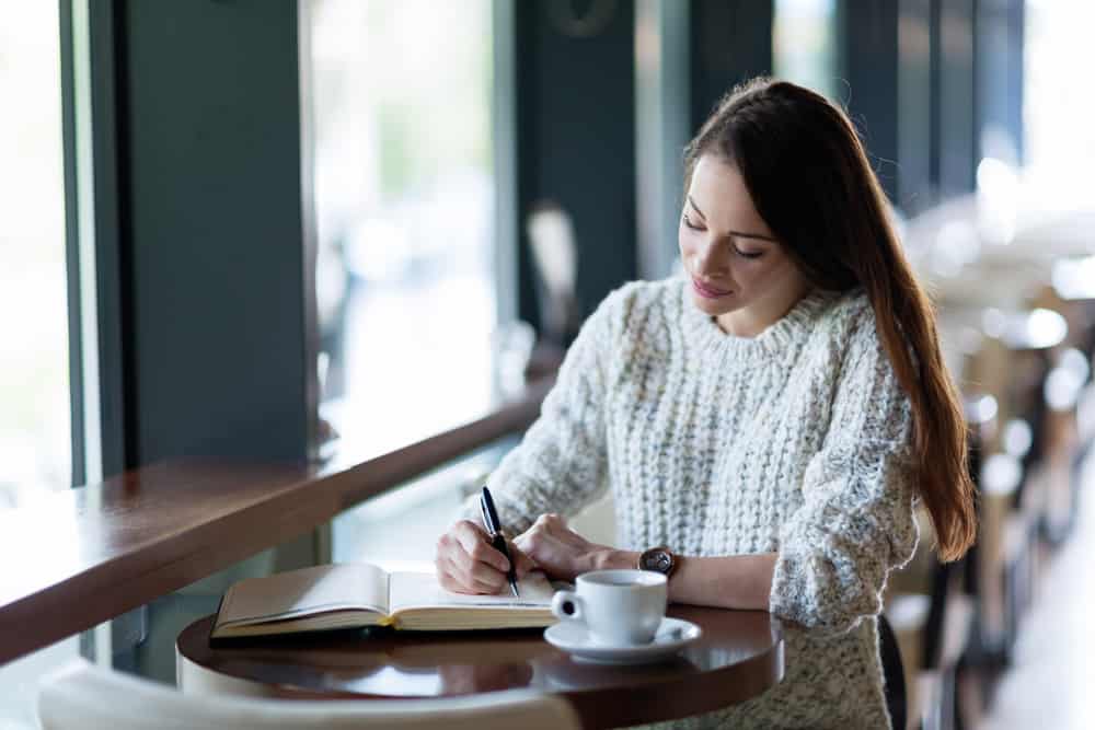 Une femme assise à une table de boire du café et d'écrire un journal