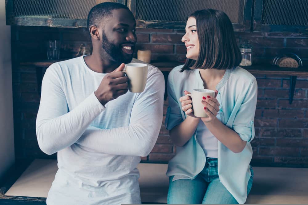 Une femme en noir et blanc souriant, boire du café dans la maison