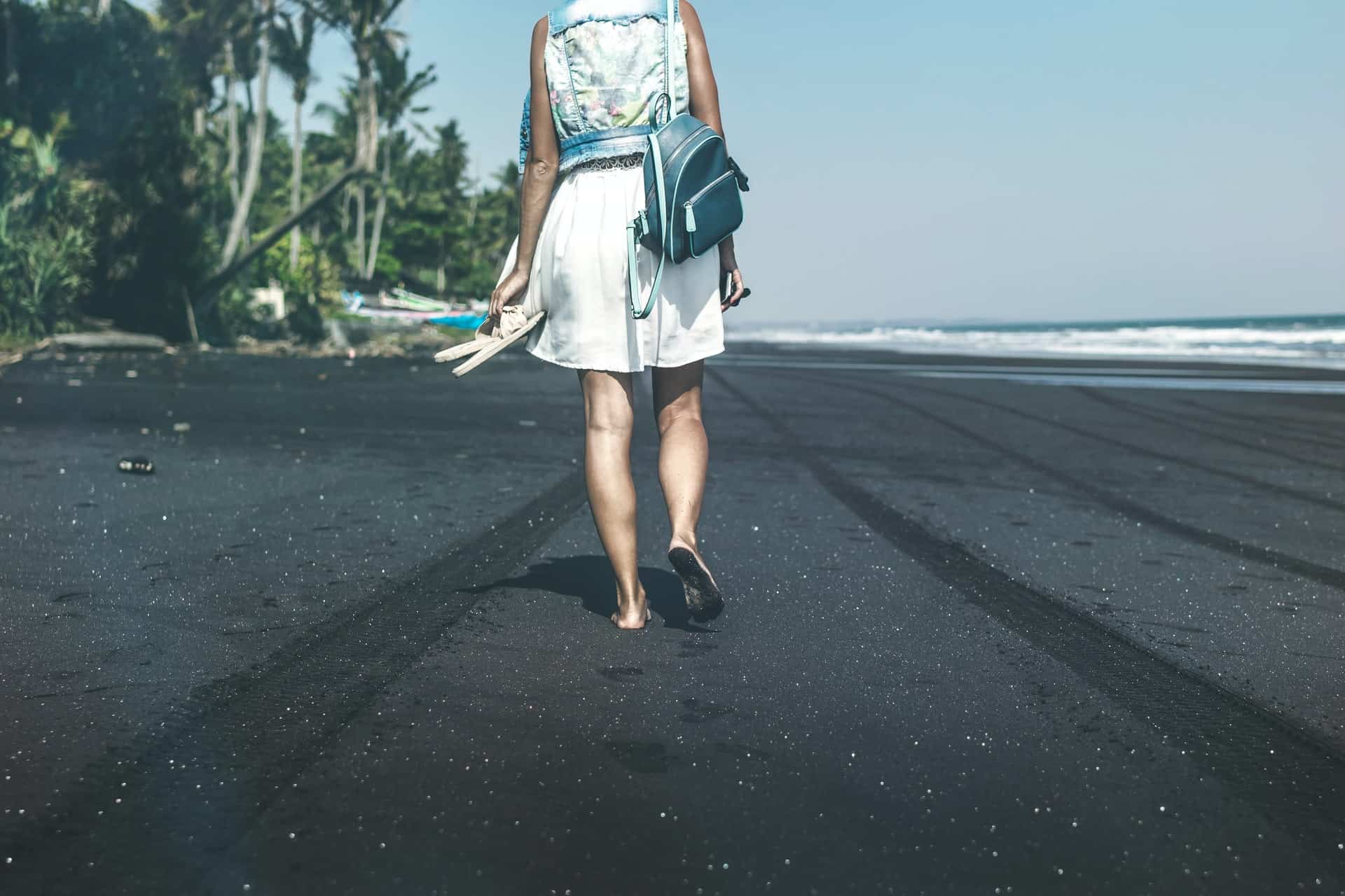 Une femme marche pieds nus sur la plage avec des pantoufles à la main