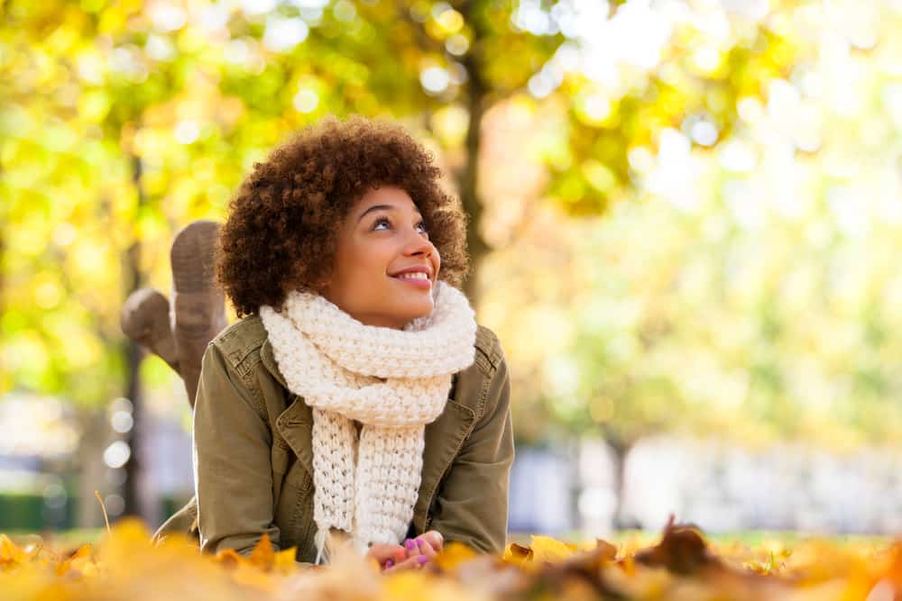 Une femme noire souriante avec un foulard blanc à l'automne se trouve sur l'herbe
