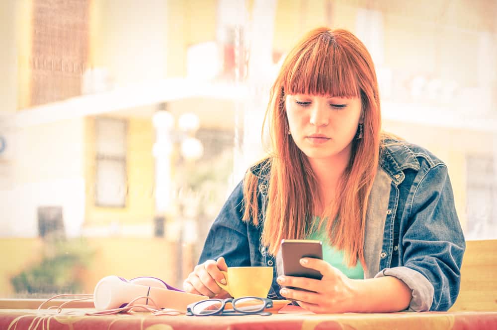 Une femme rousse est assise et utilise un smartphone autour d'un café