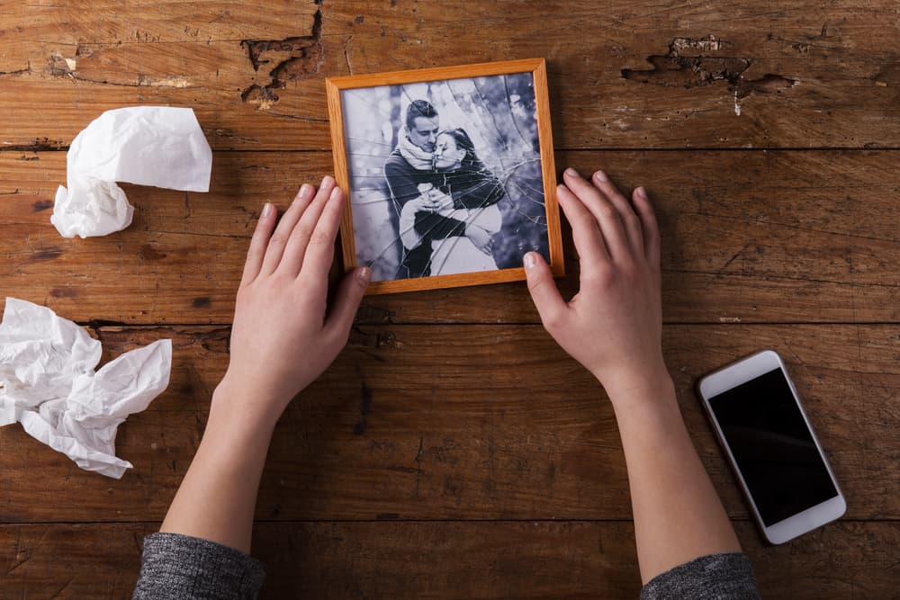 Une femme tenant une photo cassée dans ses mains sur une table à côté d'un téléphone portable et deux mouchoirs