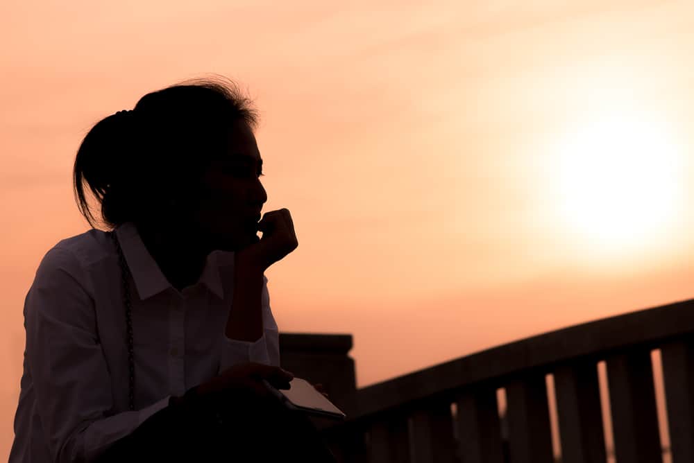 Une femme triste avec un smartphone à la main assis à l'extérieur au coucher du soleil