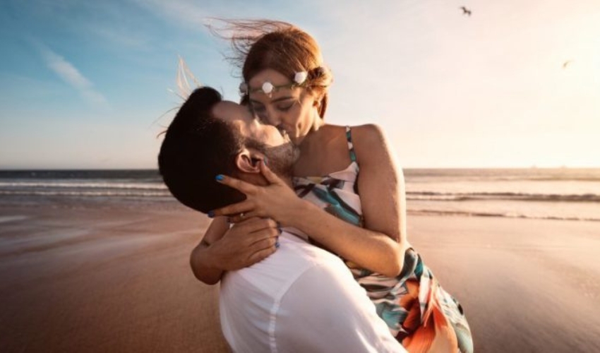 un homme porte une femme a la plage et lembrasse