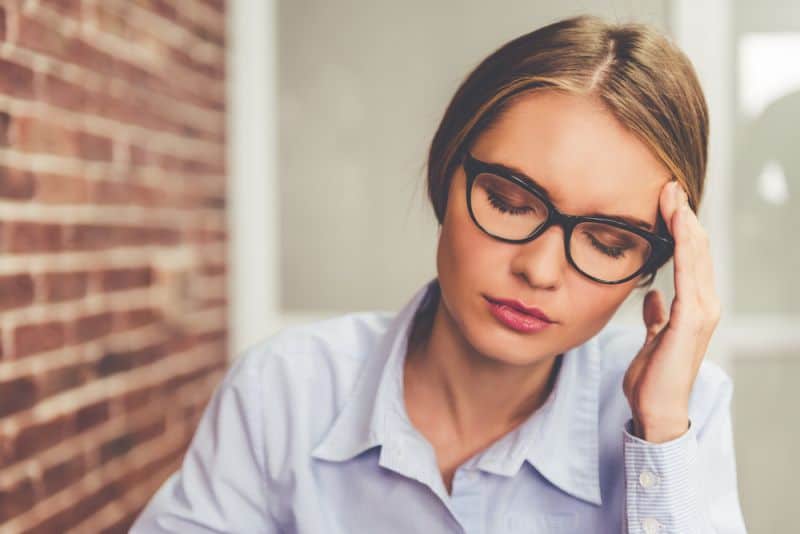 Belle femme fatiguée touche son front alors qu'il était assis les yeux fermés