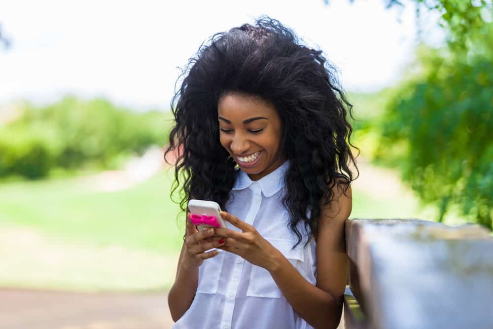 belle femme noire souriante aux cheveux luxuriants écrit des sms