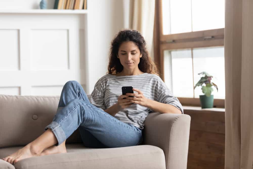 brune allongée sur le canapé et envoyant des SMS