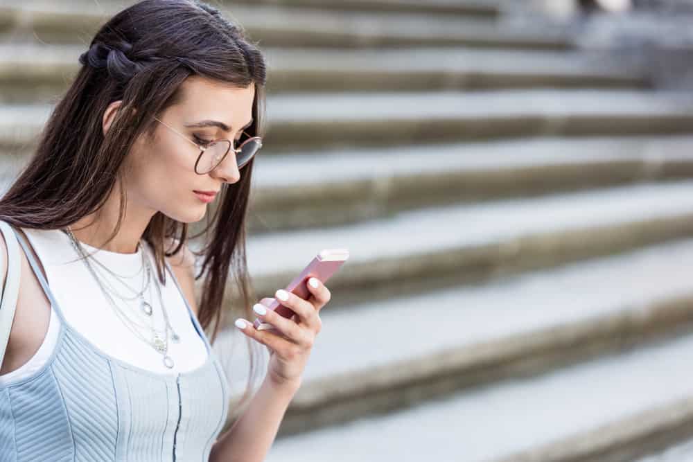brune avec des lunettes à l'extérieur par les escaliers écrit des sms