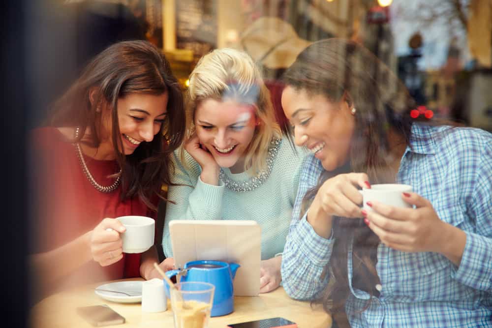 des amis autour d'un café regardent la tablette et rient