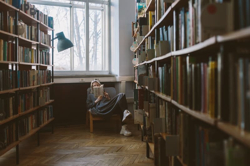 femme assise dans une bibliothèque lisant un livre
