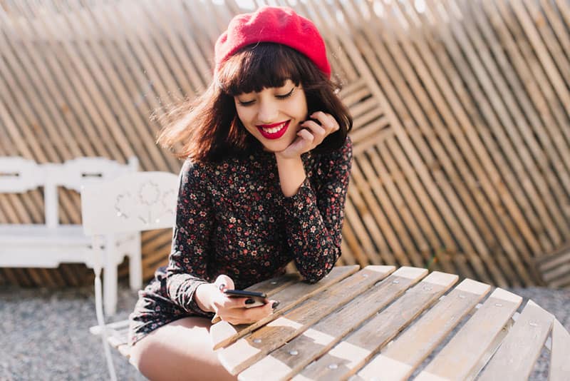 femme avec chapeau et rouge à lèvres en regardant le téléphone