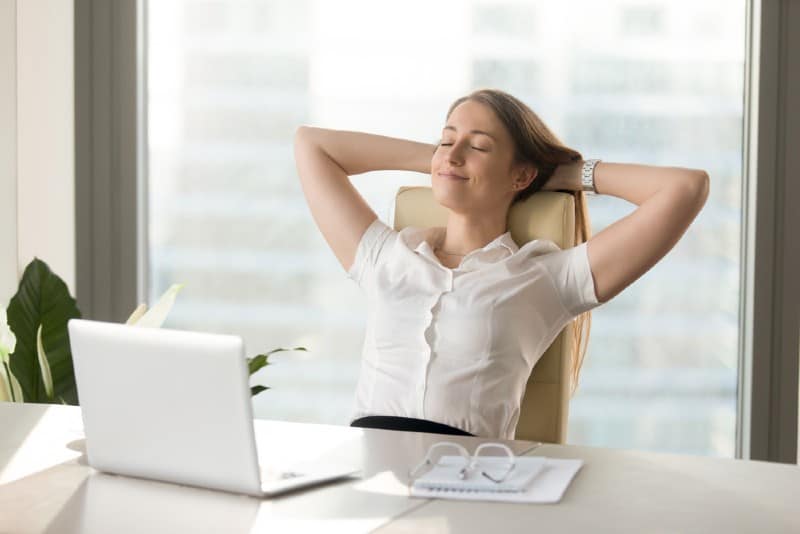 Femme d'affaires souriante calme reposant sur une chaise de bureau confortable les mains derrière la tête