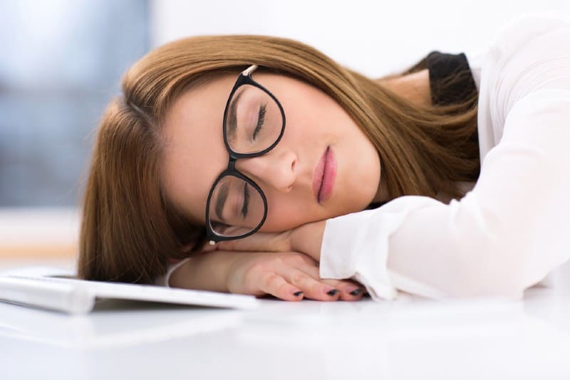 Femme d'affaires fatiguée dans des verres dormant sur la table à son lieu de travail