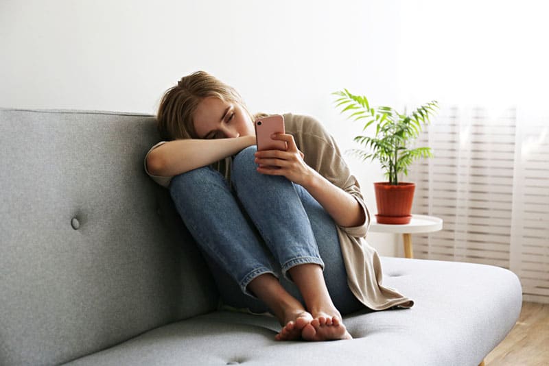 femme triste assise sur le canapé et tenant le téléphone