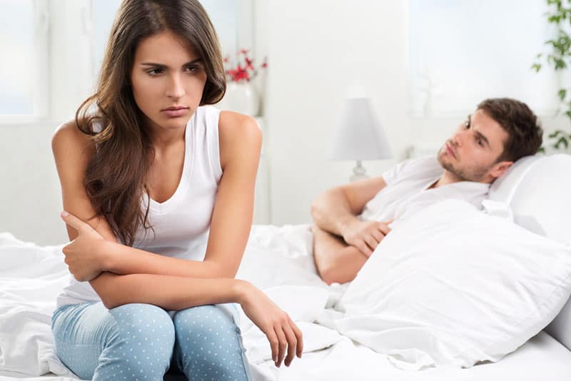 femme triste assise sur le lit tandis que l'homme couché