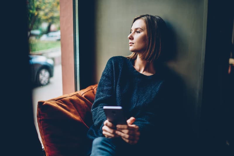 sad woman with phone sitting near window