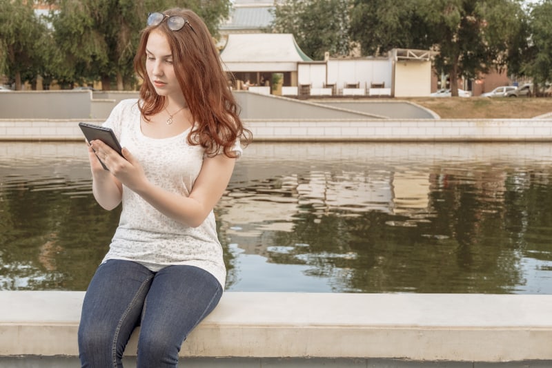 fille assise au bord du lac et utilisant un téléphone portable