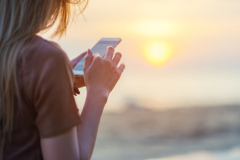 fille tapant sur un téléphone portable au coucher du soleil