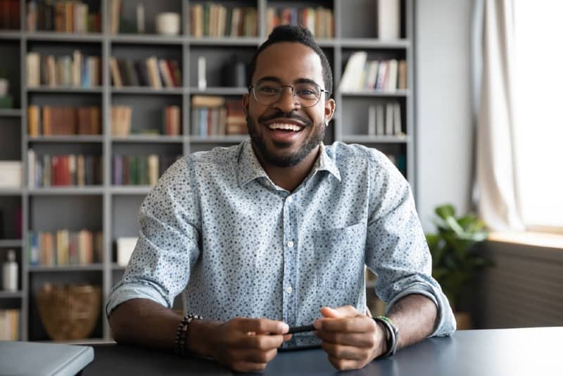  Portrait d'un homme afro-américain heureux avec des lunettes de parler et assis à un bureau