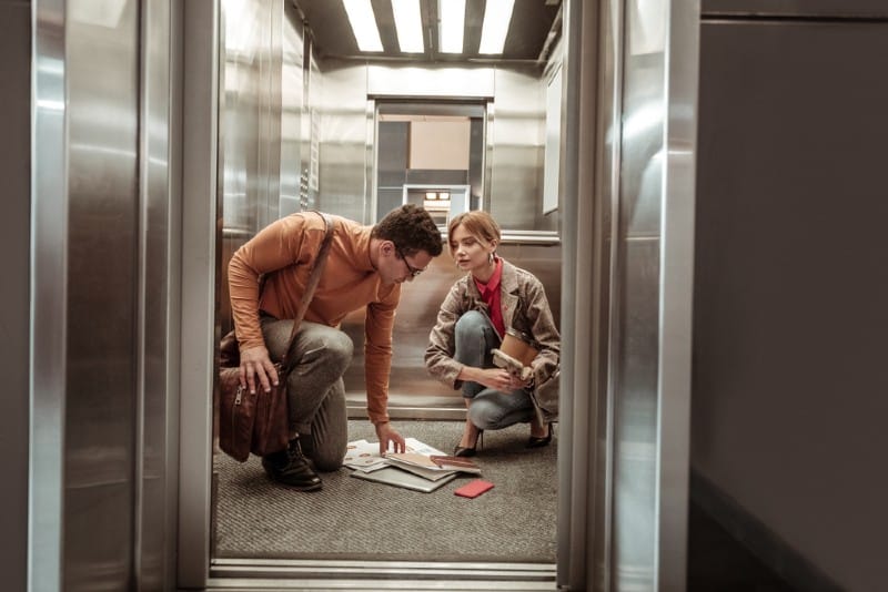un homme aidant une femme à rassembler des documents de l'étage dans l'ascenseur