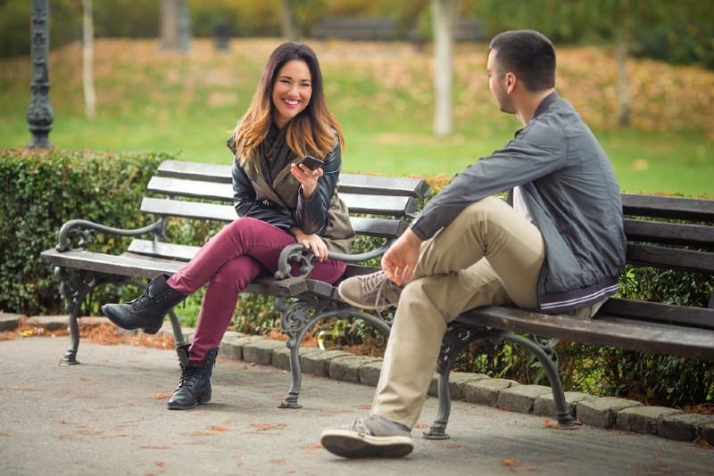 Jeune homme et femme assise sur des bancs dans un parc et parler
