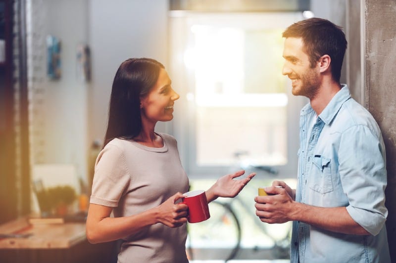 Homme et femme tenant des tasses à café et parler debout au bureau