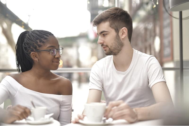 Un jeune homme et une femme se regardant tout en étant assis à une table et en buvant du café