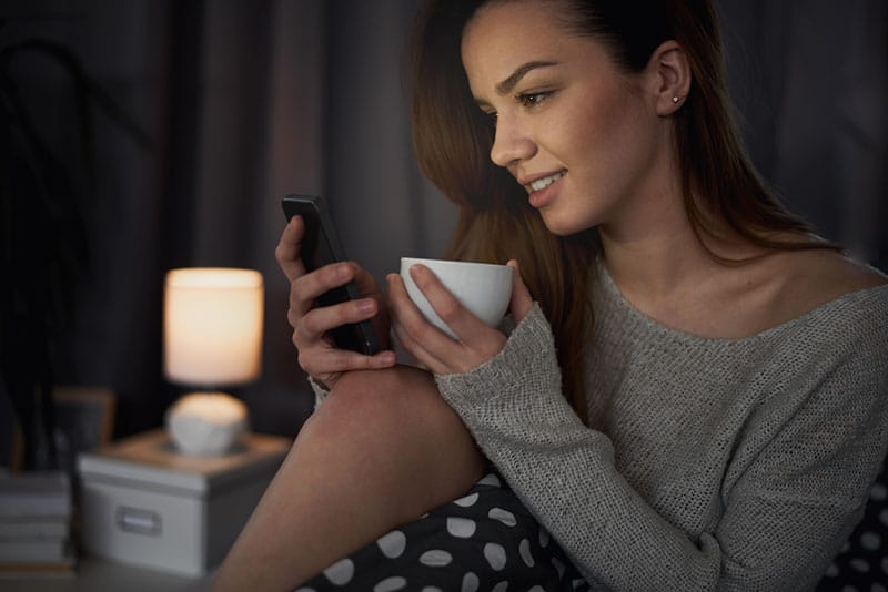 jolie jeune femme regardant téléphone et tenant une tasse de café