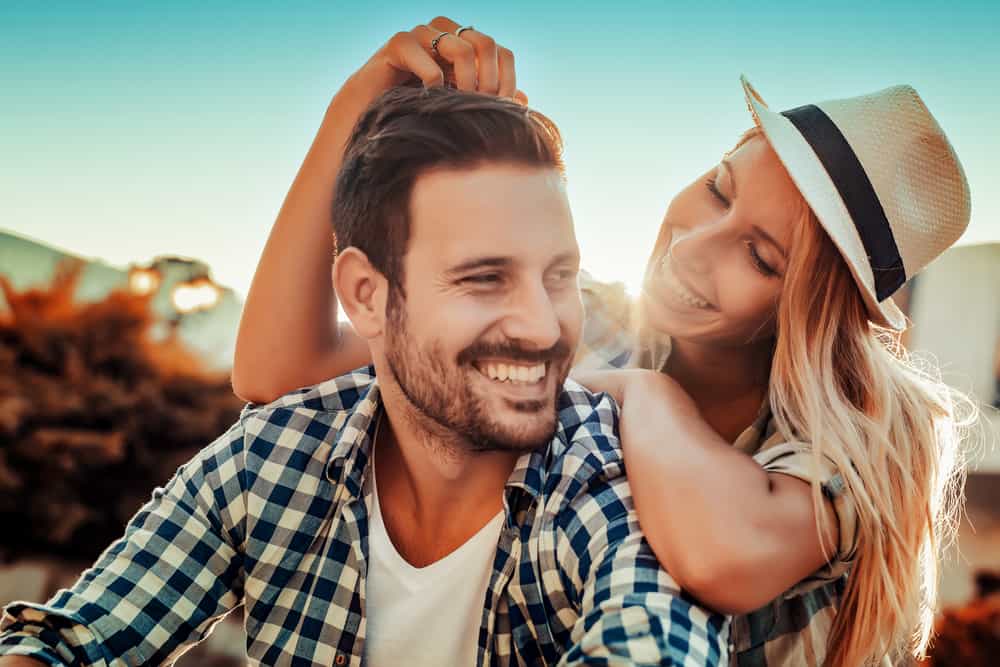 la femme au chapeau touche la tête de l'homme et rit